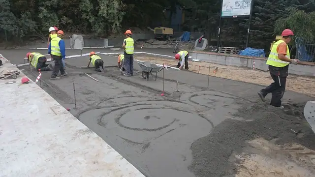 Robotnicy zacierają świeżo wylaną nawierzchnię betonową ze spiralnym wzorem dekoracyjnym na promenadzie przy molo